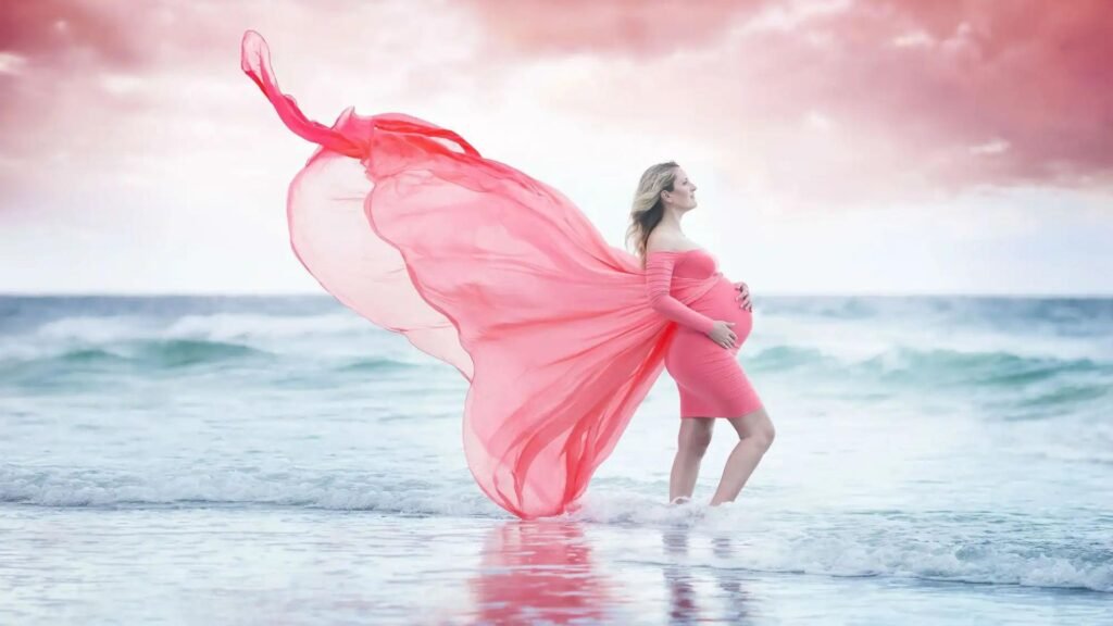 a pregnant woman standing in the sea wearing pink dress showing the concept of photography style 